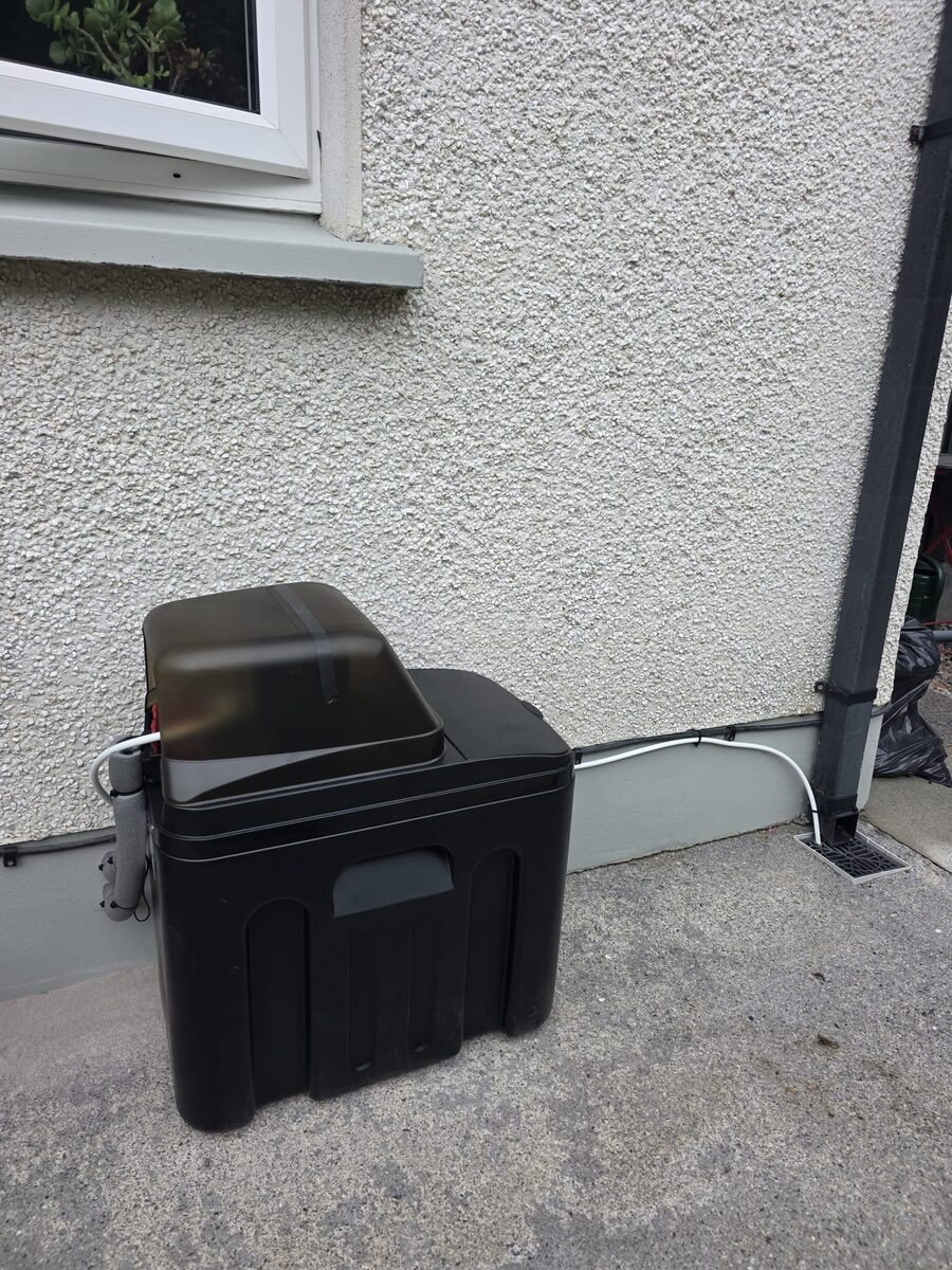 Outdoor cabinet water softener installed against a pebble-dash wall